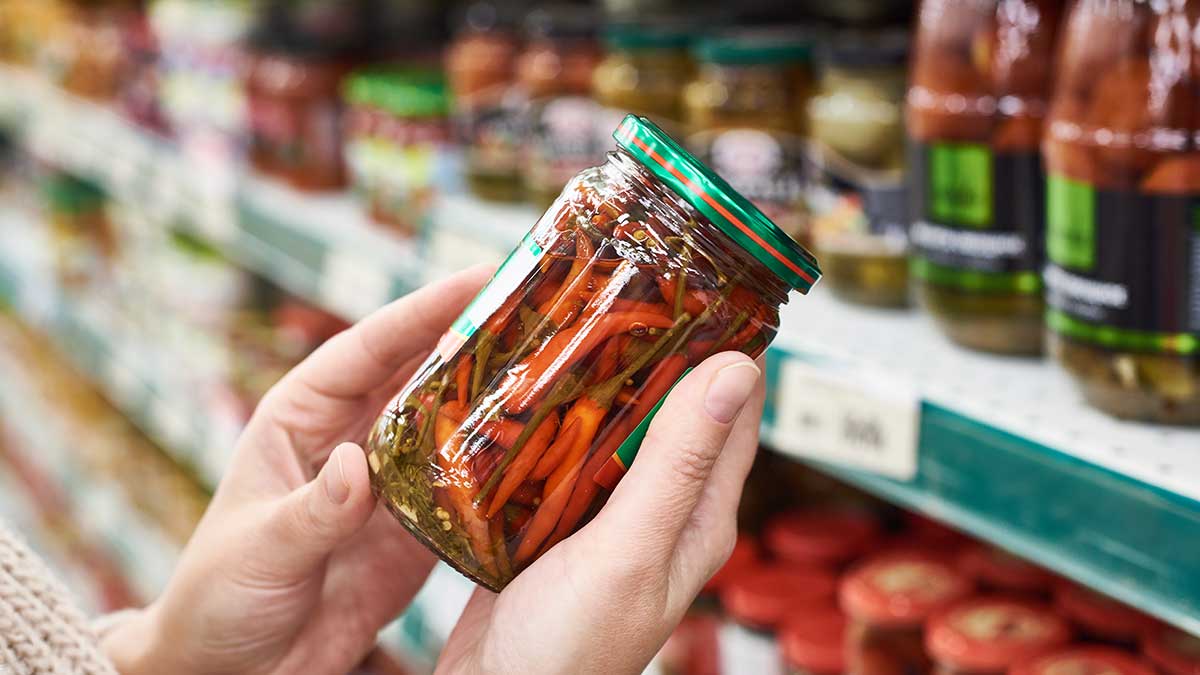 Hände halten ein Glas mit eingelegten roten Chilischoten