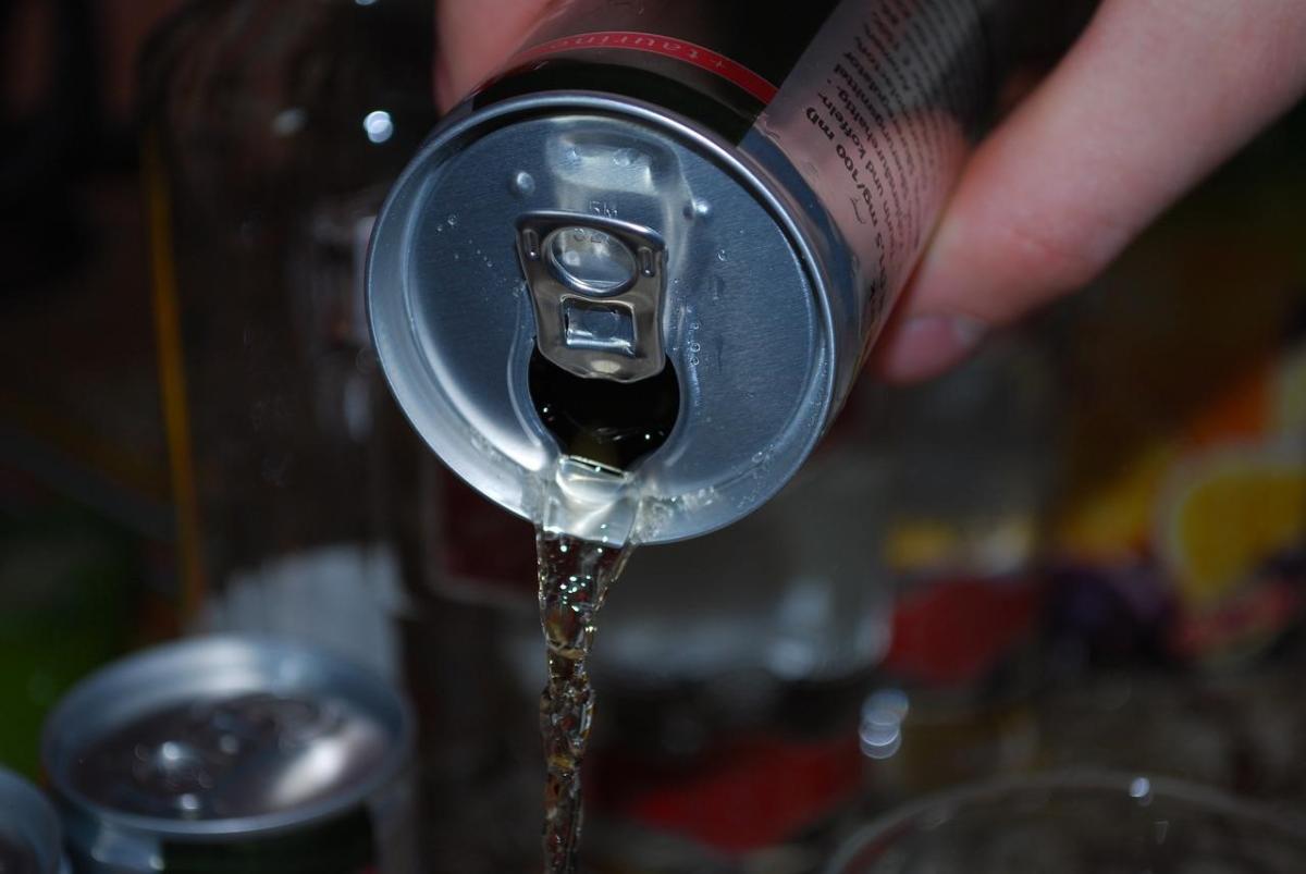 Jemand gießt ein Getränk aus einer Getränkedose in ein Glas