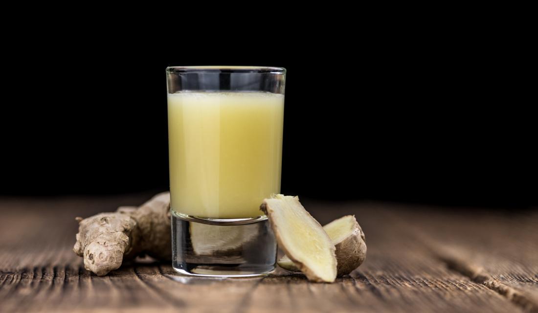 Shotglas mit Ingwergetränk auf Tischplatte vor dunklem Hintergrund