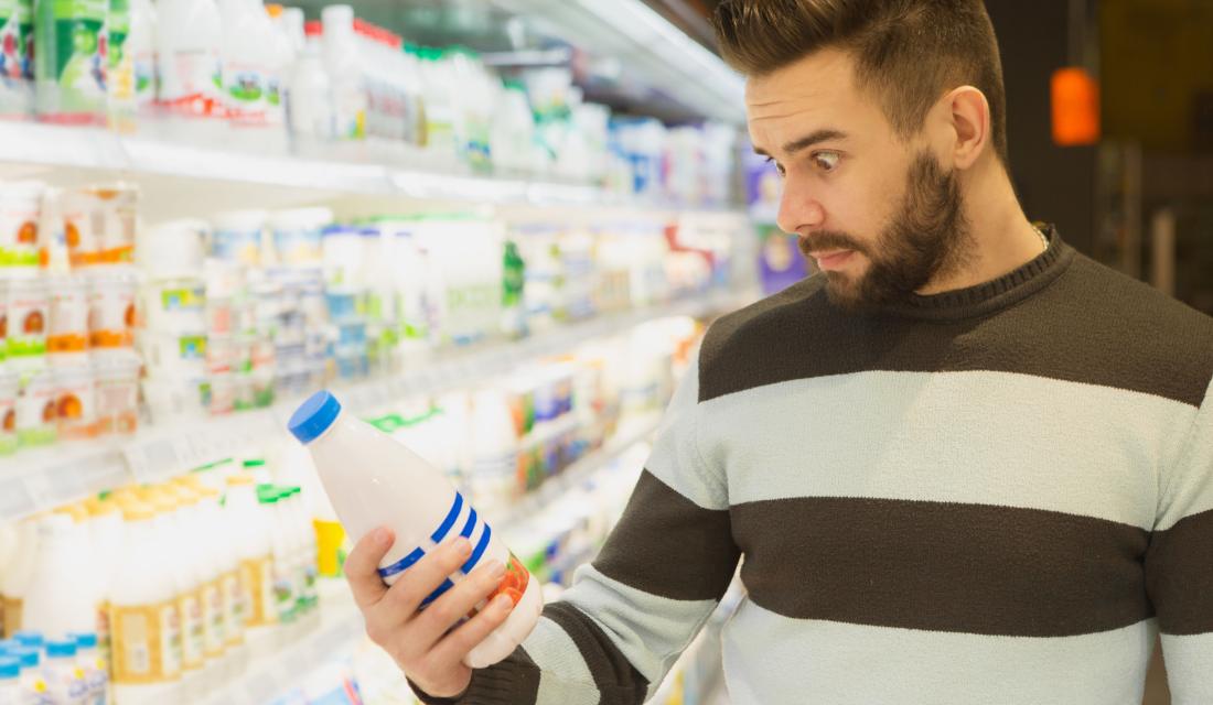 Mann mit überraschtem Gesichtsausdruck liest Verpackungstext im Supermarkt