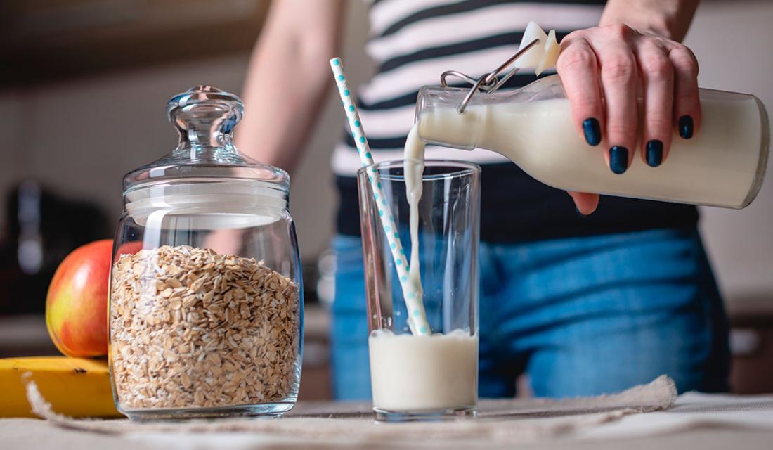 Frau gießt Milch oder Milchersatz aus einer Glasflasche in ein Glas
