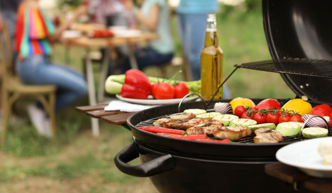 Ein Grill mit Gemüse und Fleisch steht auf einer Wiese.