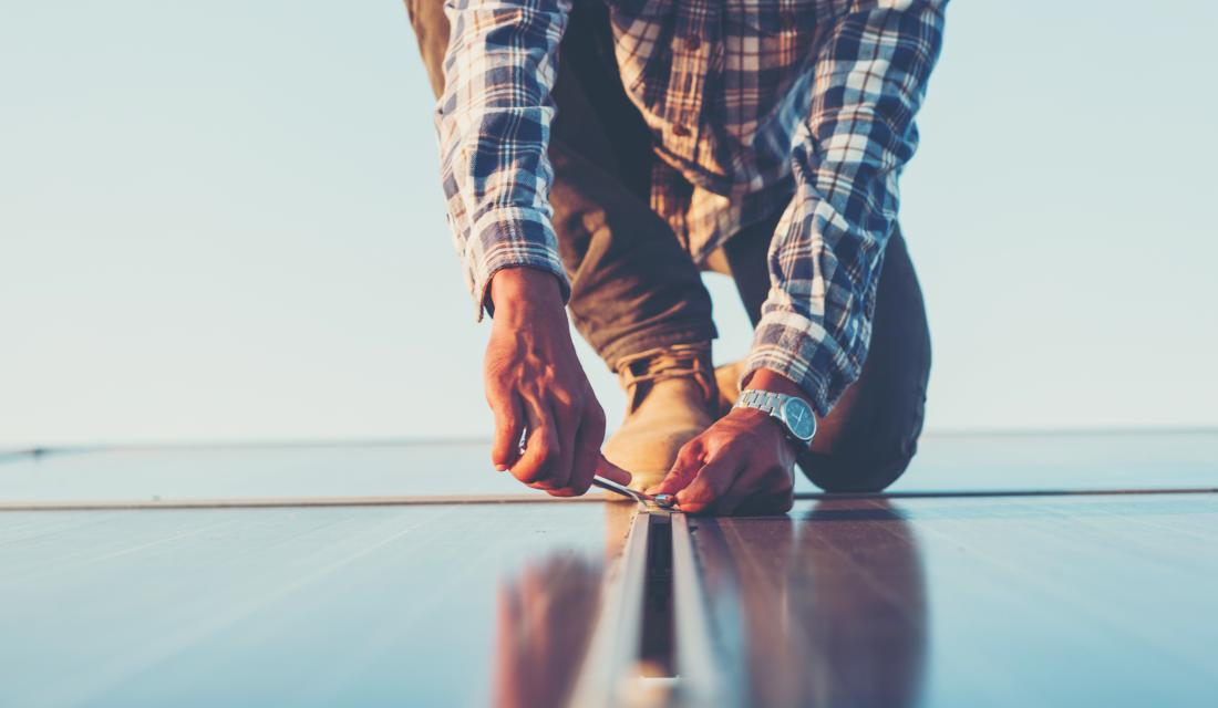 Person schraubt PV-Modul auf Dach fest