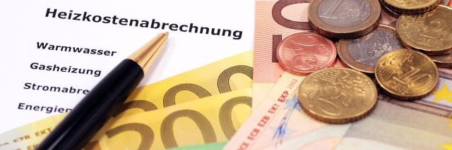 Auf einer Heizkostenabrechnung liegen Euroscheine und -Münzen und ein Kugelschreiber.