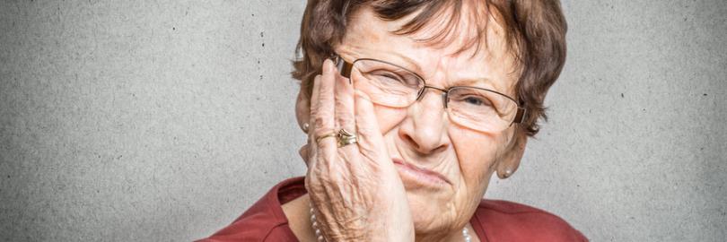 Seniorin hält sich die Wange, weil ihr Zahnersatz Beschwerden verursacht.