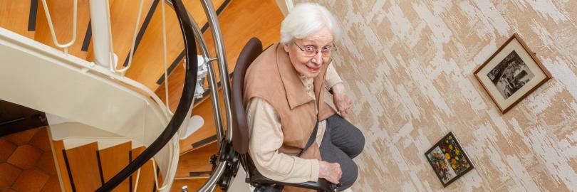 Eine ältere Dame fährt im Treppenhauf mit einem Treppenlift