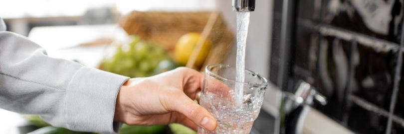 Jemand lässt am Waschbecken Wasser in ein Glas laufen.