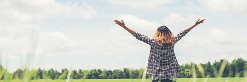 Eine junge Frau steht mit offenen Armen auf einem Feld.