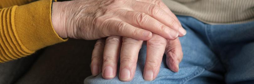 Die Hand einer Person auf der Hand einer anderen Person auf einem Oberschenkel.