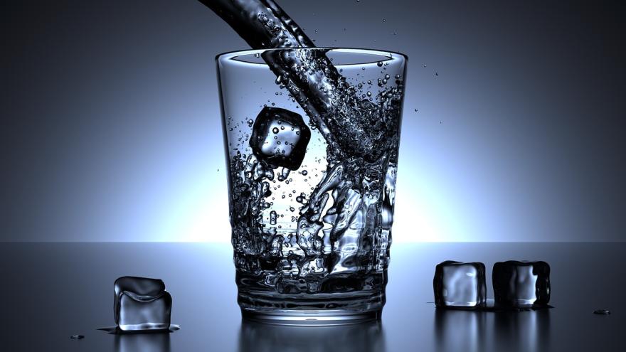 Wasser wird in ein Glas mit Eiswürfeln eingeschenkt