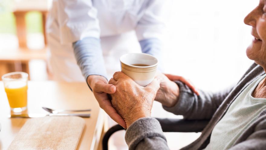 Pflegerin reicht Glas an Seniorin