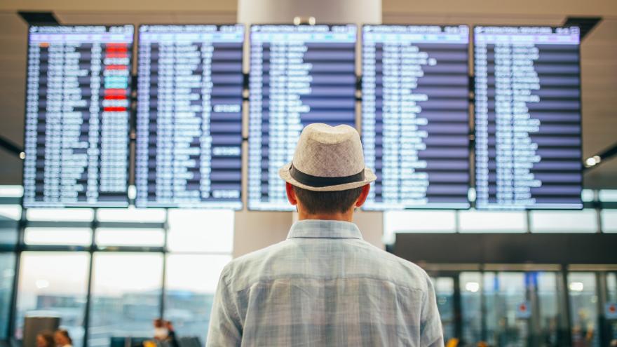 Mann steht vor Anzeigtafel am Flughafen