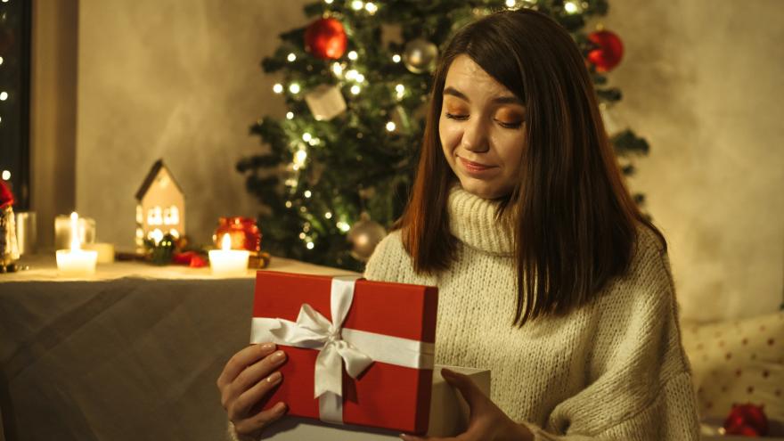 Frau betrachtet enttäuscht Geschenk vor Weihnachtsbaum