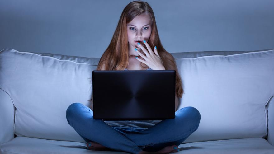 Junge Frau blickt erschrocken auf Laptop