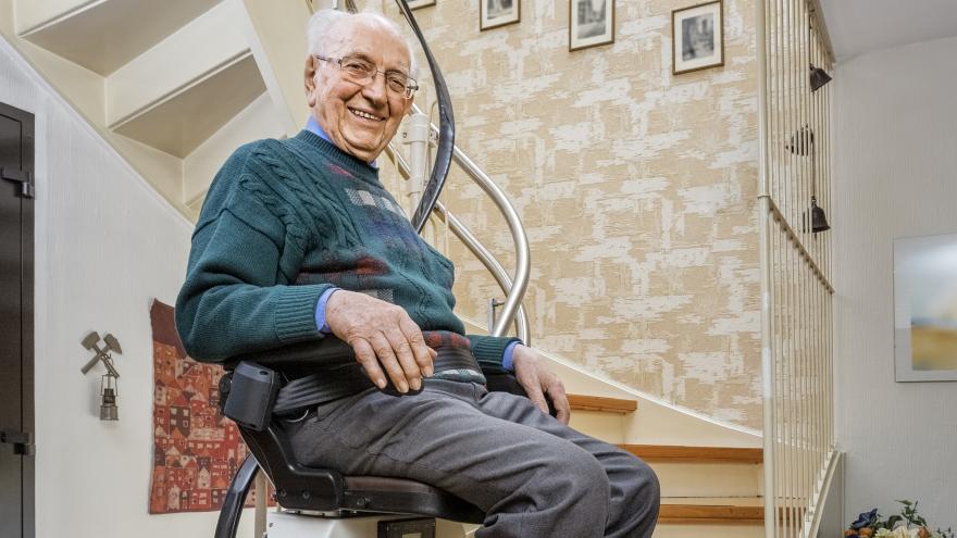 Älterer Mann sitzt auf einem Treppenlift und lächelt in die Kamera