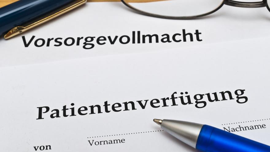 Ausdruck einer Patientenverfügung und eines Vorsorgevollmacht neben zwei Stiften und einer Brille auf einem Tisch