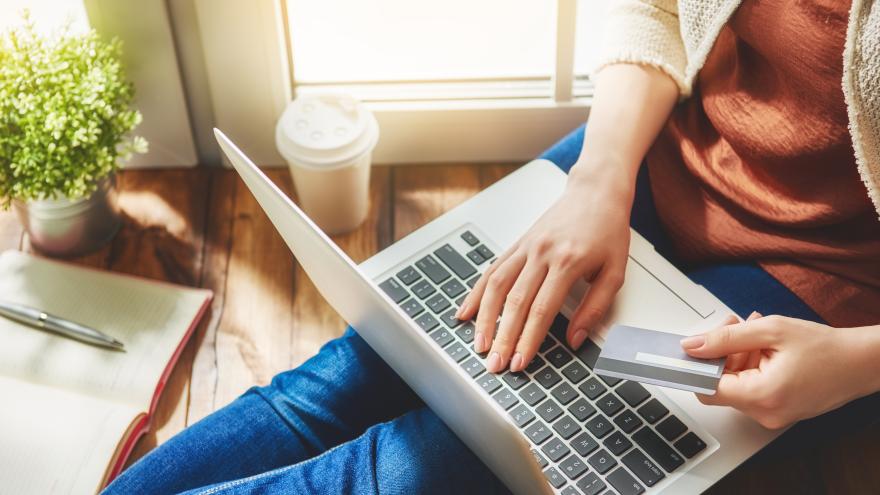 Mann sitz auf der Couch und bestellt mit seinem Laptop online. In der linken Hand hält er eine Kreditkarte