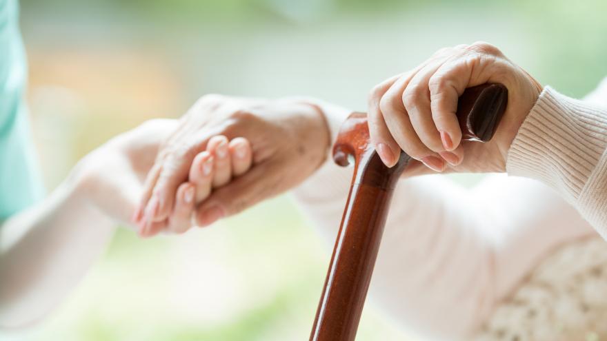 Pflegerin hält die Hand einer Seniorin mit Gehstock in Nahaufnahme