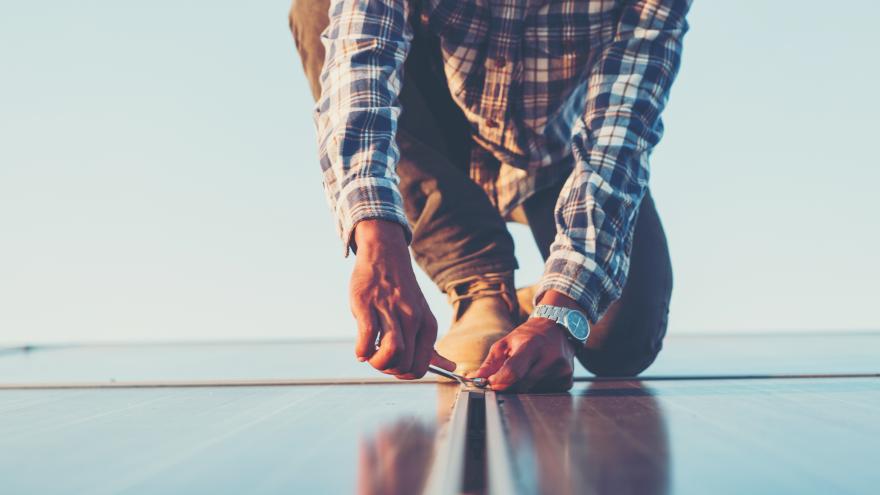 Knieender Handwerker bei der Montage von Photovoltaik-Paneelen
