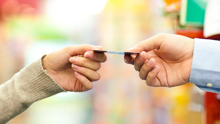 Frau reicht einem Verkäufer im Supermarkt eine Karte