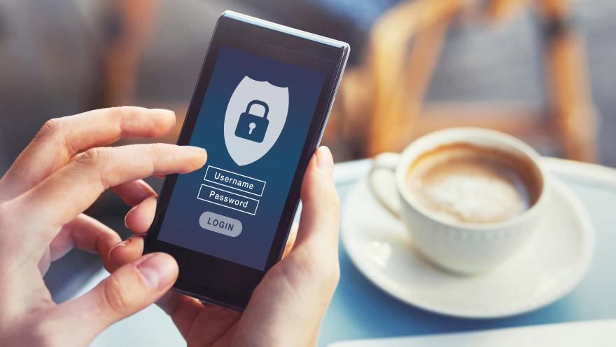 Hände mit Smartphone auf dem eine Eingabeaufforderung für ein Passwort angezeigt wird in einem Café