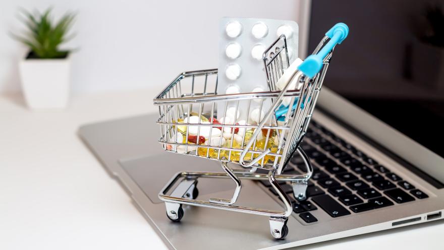 Ein Miniatureinkaufswagen ist mit Tabletten gefüllt und steht auf einem Laptop