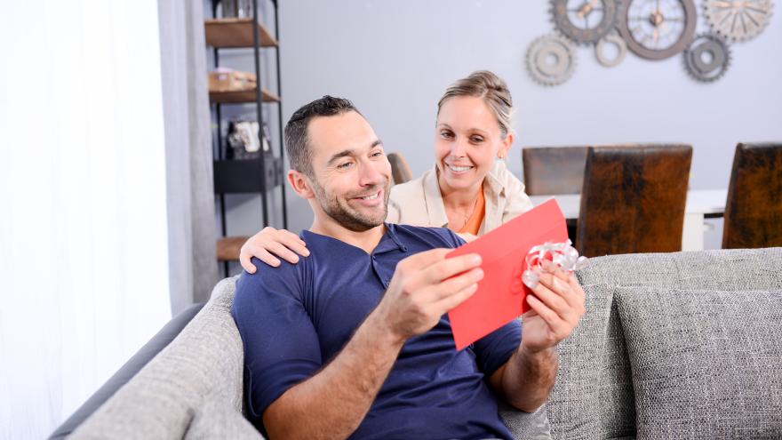 Frau überreicht Ihrem Partner einen Gutschein ind Geschenkverpackung