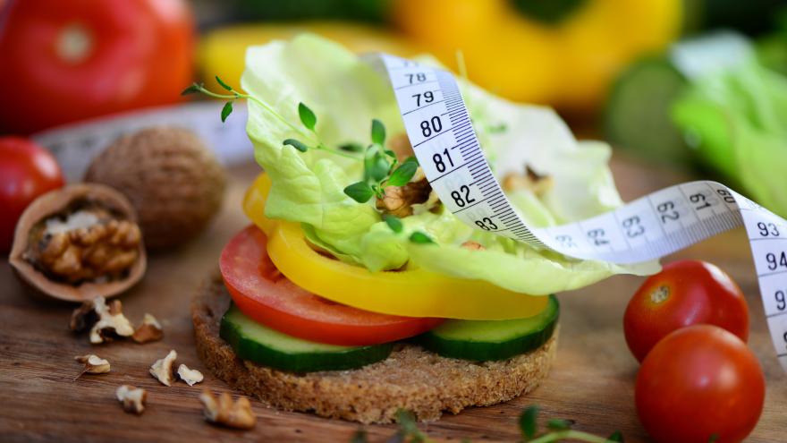 Maßband liegt auf einem Brot, das mit Salat und Gemüse belegt ist