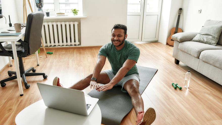 Blick auf einen Mann beim Online-Fitnesstraining mit dem Laptop im eigenen Wohnzimmer