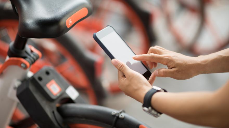 Eine Hand hält ein Smartphone an ein Fahrrad eines Bikesharing-Anbieters, um es zu entsperren