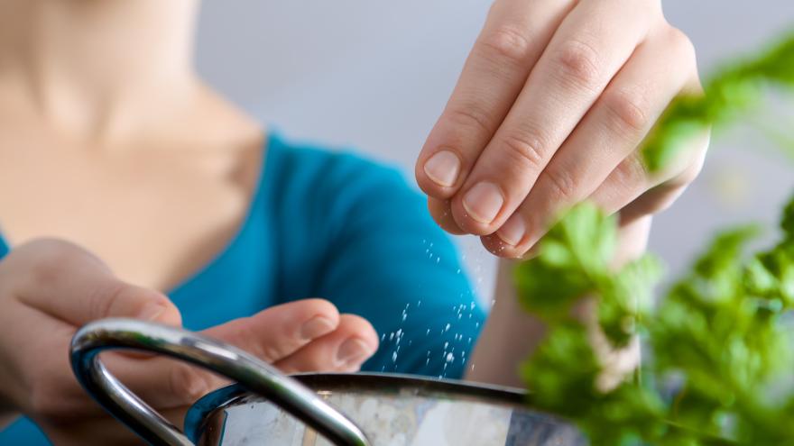 Frau streut Salz aus ihrer Hand in einen Topf