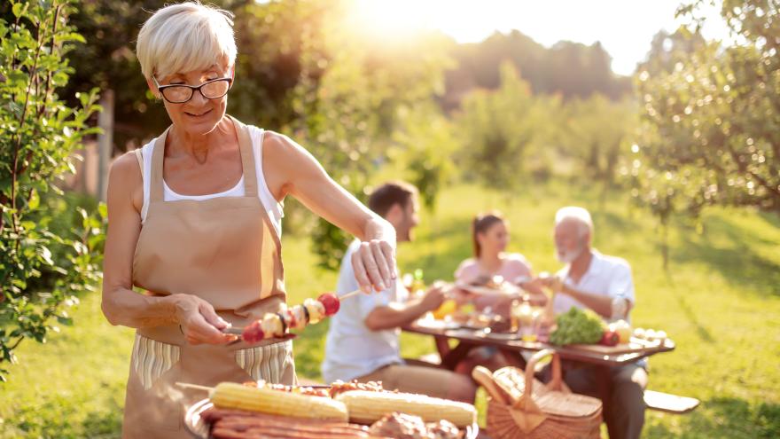 Ältere Frau beim Grillen mit Familie im Hintergrund