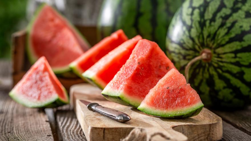 Aufgeschnittene Wassermelone liegt auf einem Gartentisch. Mehrere ganze Melonen liegen im Hintergrund