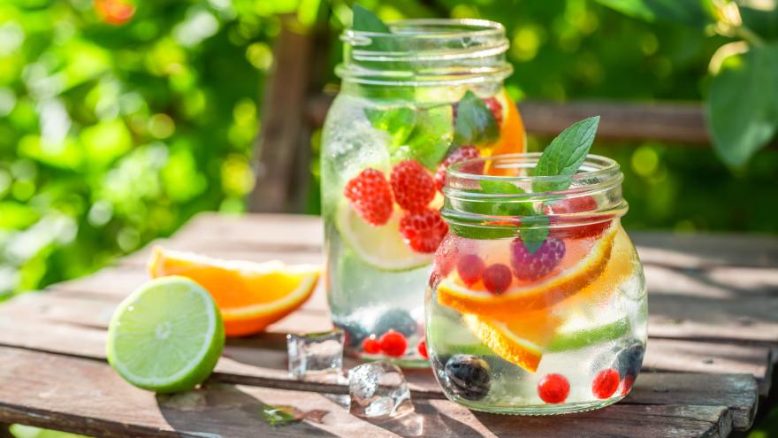 Verschiedene Gläser mit Wasser und Früchten stehen auf einem Gartentisch
