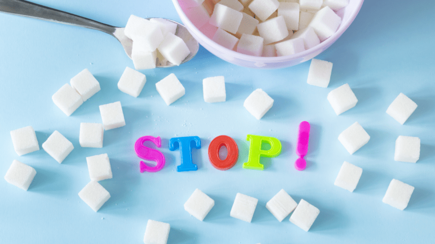 Zwischen vielen Zuckerwürfeln liegen Buchstaben auf einem Tisch, die das Wort "Stop!" bilden.