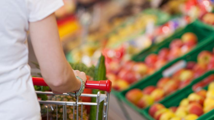 Frau schiebt einen Einkaufswagen neben dem Obstregal eines Supermarkts