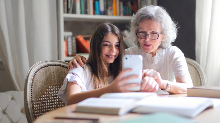 Seniorin und Enkelin sitzen am Tisch und benutzen gemeinsam ein Smartphone