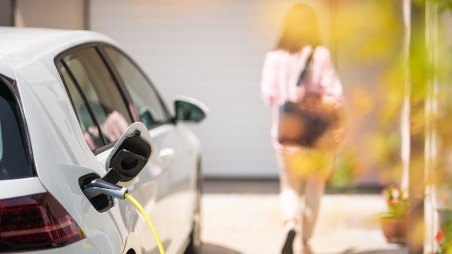 Eine Frau geht von ihrem Elektroauto weg, das an den Strom angeschlossen ist.