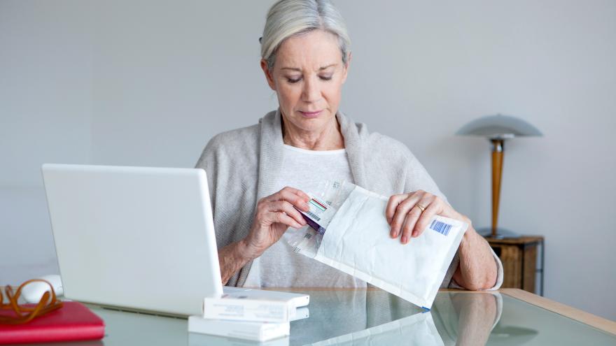 Eine Frau packt vor dem Laptop Medikamente aus.