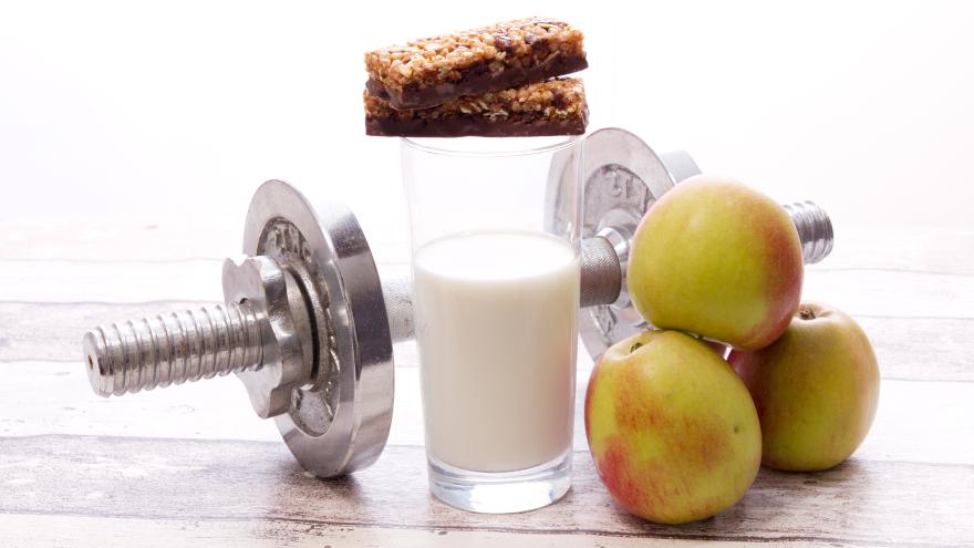 Hanteln mit einem Glas Milch, Äpfeln und einem Riegel.