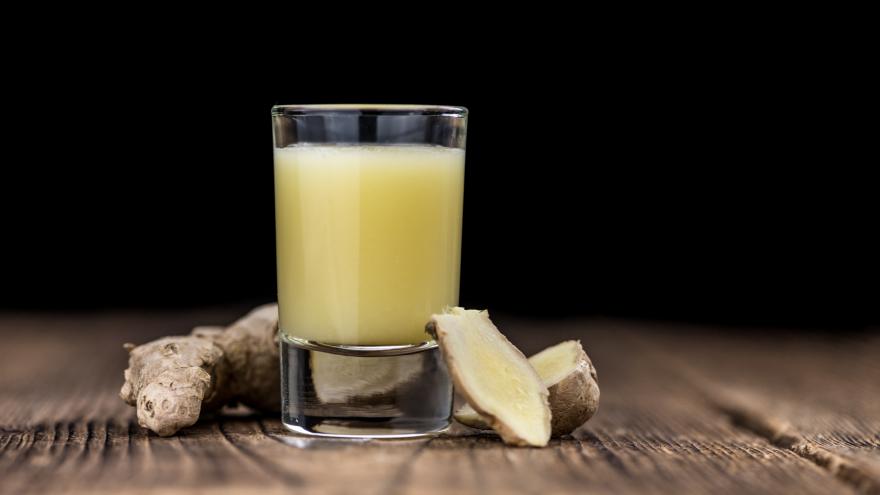 Shotglas mit Ingwergetränk auf Tischplatte vor dunklem Hintergrund