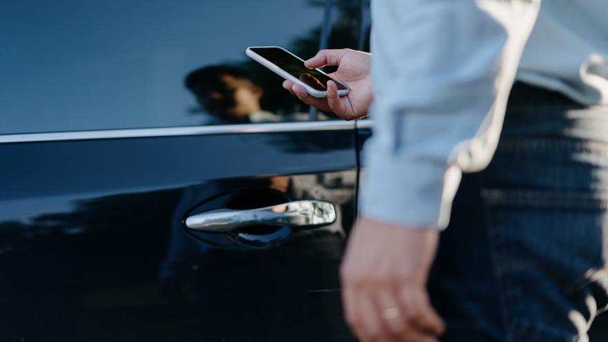 Mann beim Öffnen der Tür eines Autos mit seinem Smartphone