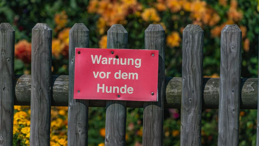 Ein Warnschild vor dem Hund hängt am Gartenzaun.