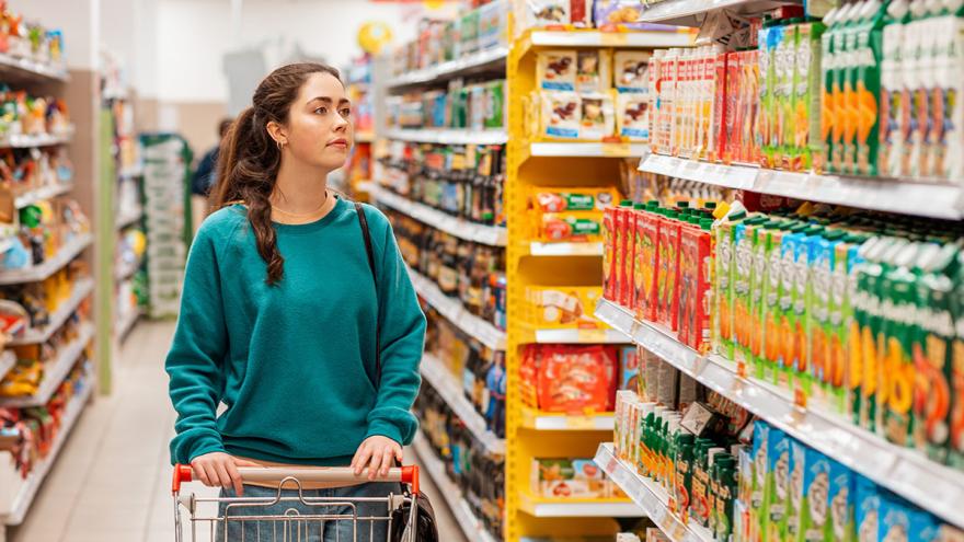 Frau steht mit Einkaufswagen vor Saftregal im Supermarkt