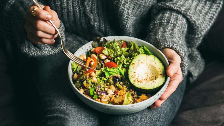 Frau hält eine Schüssel mit einem veganen Gericht in einer Hand und in der anderen eine Gabel