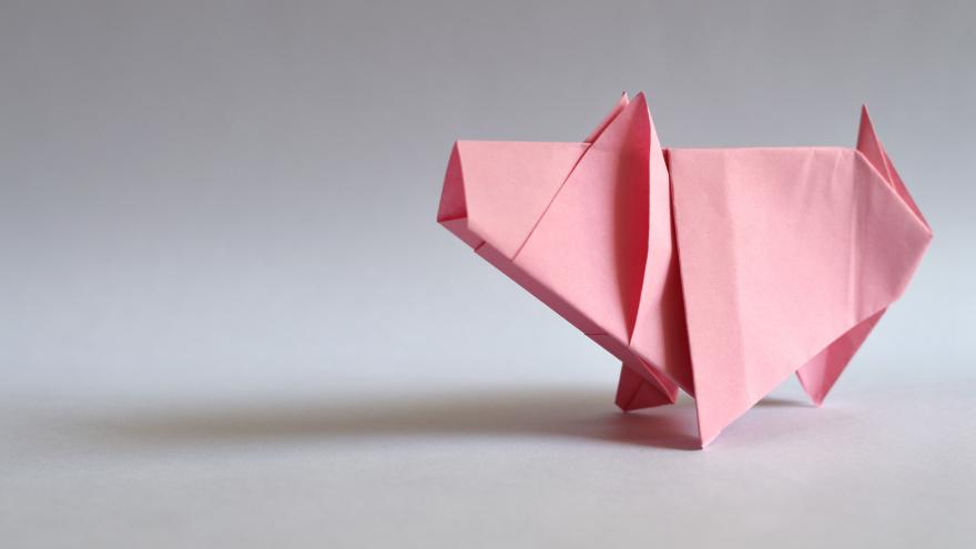 Ein rosa Schwein, gefaltet aus Papier von einem grauen Hintergrund