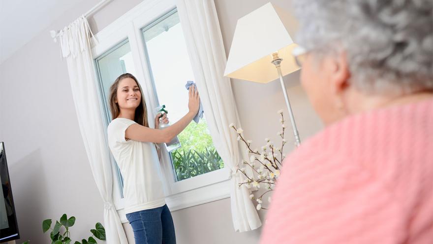 Putzkraft beim Reinigen der Fenster einer Seniorin