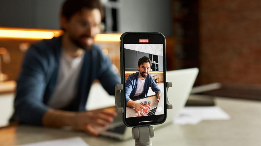 Smartphone auf Stativ nimmt an einem Laptop sitzenden Mann auf