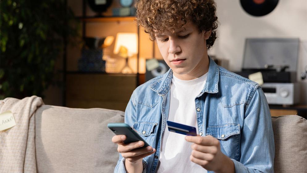 Teenager beim Online-Shopping mit Smartphone und Kreditkarte auf dem Sofa