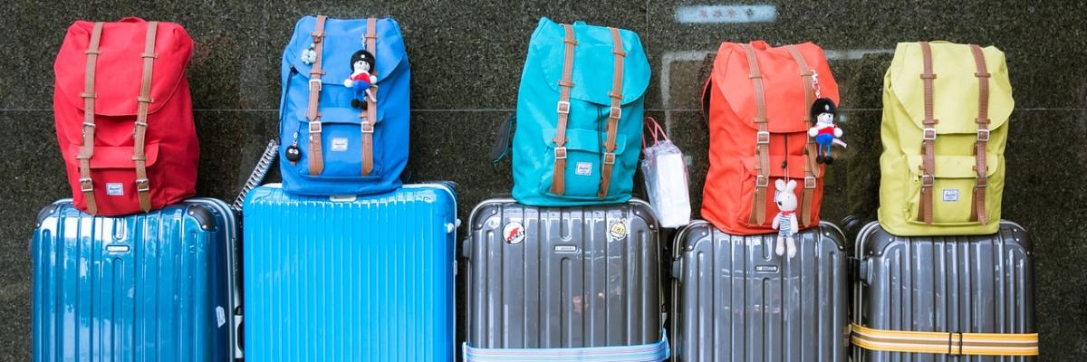 Fünf nebeneinanderstehende Koffer mit daraufstehenden Rucksäcken
